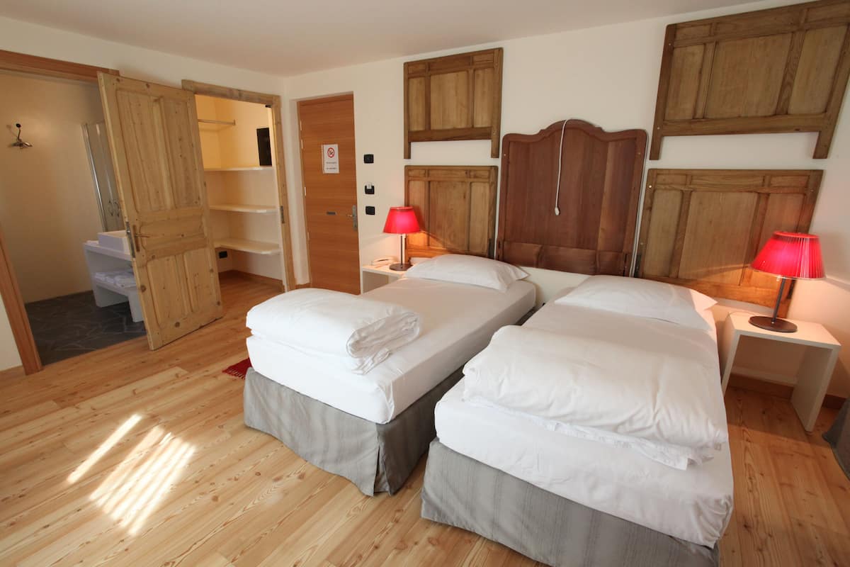 A room with two beds, wooden flooring, and a wardrobe.