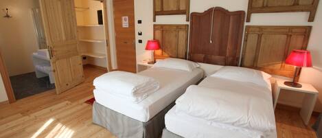 A room with two beds, wooden flooring, and a wardrobe.