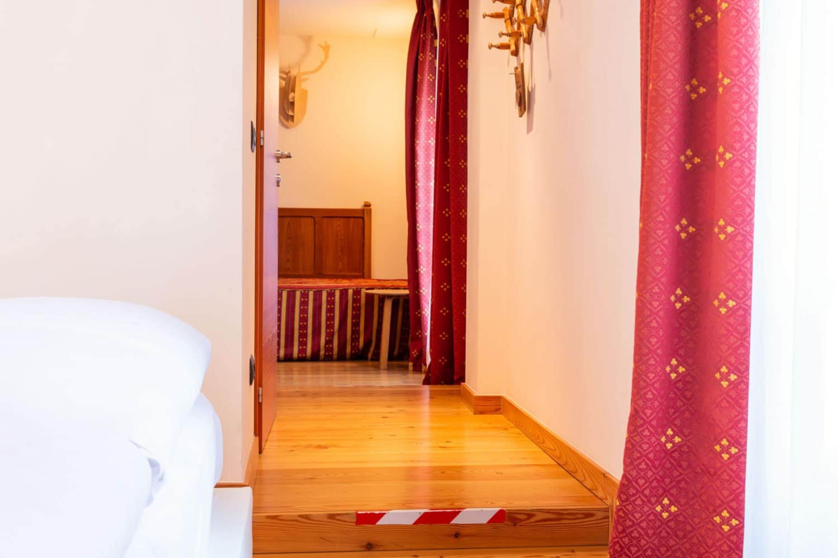 Una habitación de hotel con piso de madera, una cama, cabecera de madera y cortina roja con estampado.
