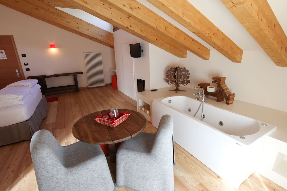 A bedroom with a bed, a wooden ceiling, a white bathtub, and a small table with chairs.