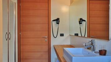 A bathroom with wooden doors, a white sink, a mirror, and a hairdryer mounted on the wall.