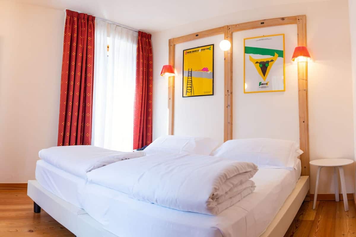 A double bed with white linens, a wooden headboard, two wall-mounted lamps, and a small round table beside the bed.