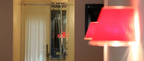 A room with a door leading to a bathroom, a red lamp, and a window with blinds.