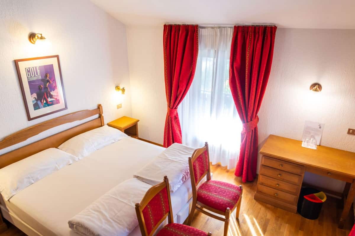 A hotel room with a bed, two chairs, a desk, and a trash bin.