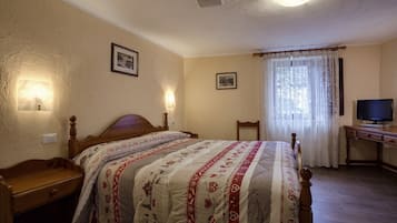 A bedroom with a wooden bed, a nightstand, a desk with a television, and two wall-mounted lamps.