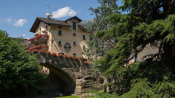 A historic building with a stone bridge, lush greenery, and a clear blue sky. - Hotel Cecchin (Aosta)