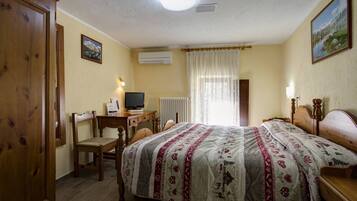 A hotel room with a bed, a desk with a computer, a chair, a radiator, and a window with curtains.