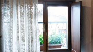 A room with a window, a curtain, and a view of a balcony with plants. - Hotel Cecchin (Aosta)