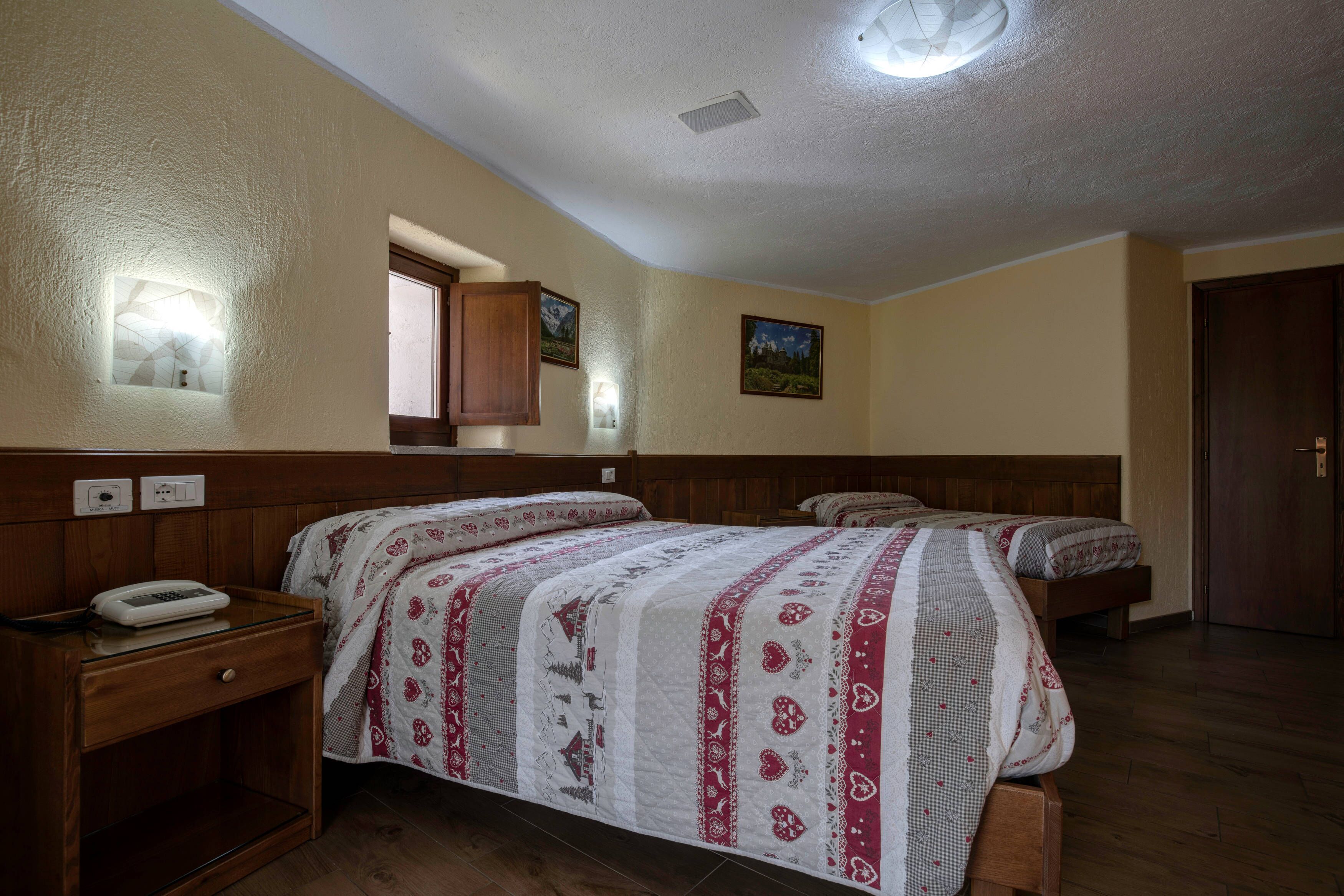 A hotel room with two beds, wooden headboards, a bedside table with a phone, and wall-mounted lights.