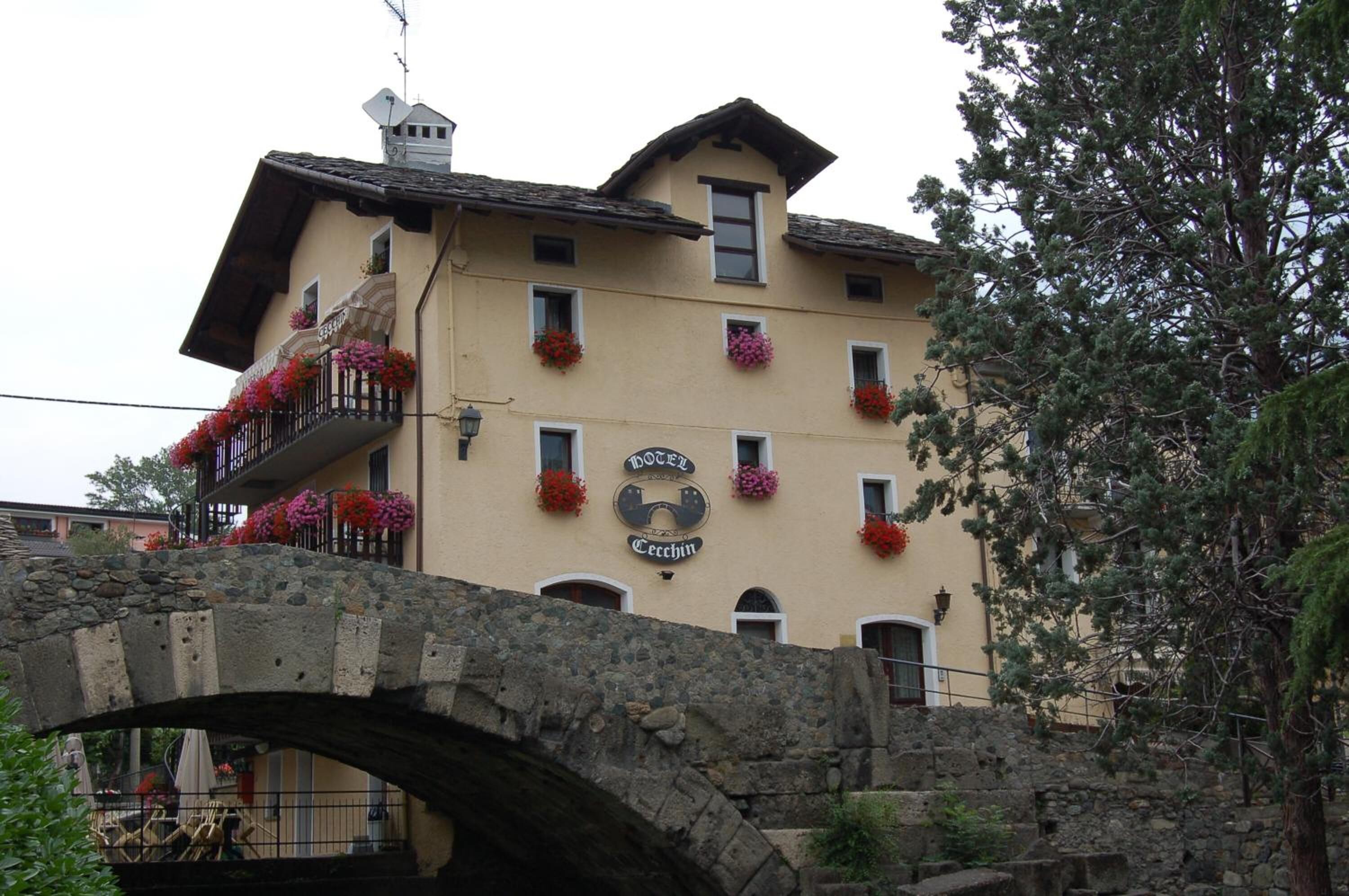 A building with a sign reading "Hotel Cecchin" and a stone bridge in front.