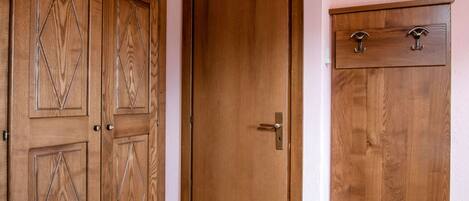 A room with wooden double doors, a single door, and a wooden cabinet with a glass shelf.
