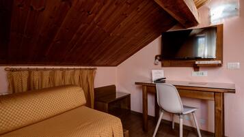 A bedroom with a wooden ceiling, a bed with a patterned bedspread, a desk with a chair, and a television mounted on the wall.