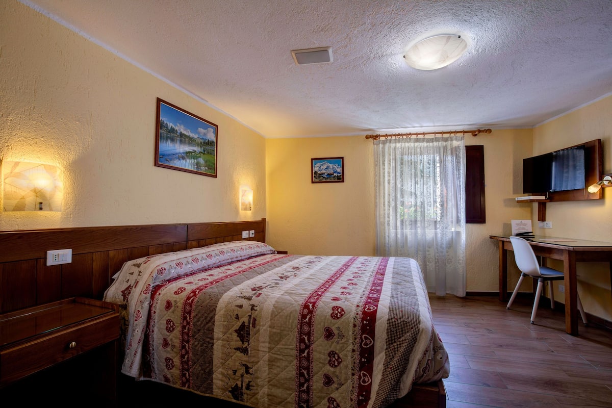 Une chambre à coucher comprenant un lit, un bureau, une chaise, un téléviseur et deux lampes fixées au mur.