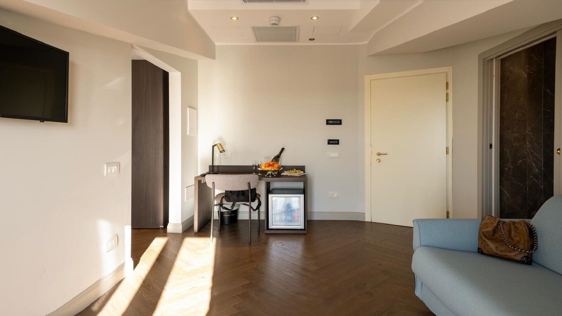 Een moderne woonkamer met een bank, een kleine tafel met een fles en glazen, een stoel en een minibar.
