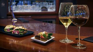 Uma área de bar com balcão de madeira, duas taças de vinho e um prato de petiscos.