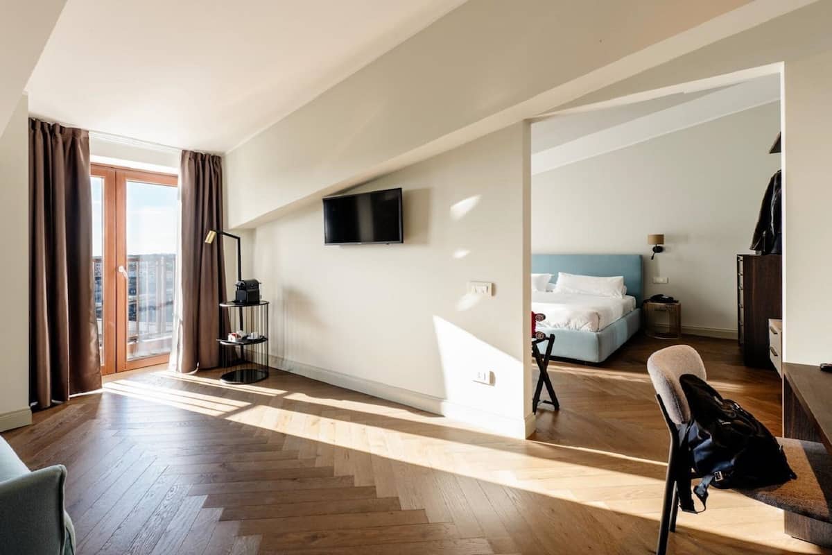 A modern hotel room with a large window, a flat-screen TV, a bed, a desk, and a chair.