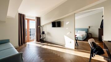 A modern hotel room with a large window, a flat-screen TV, a bed, a desk, and a chair.