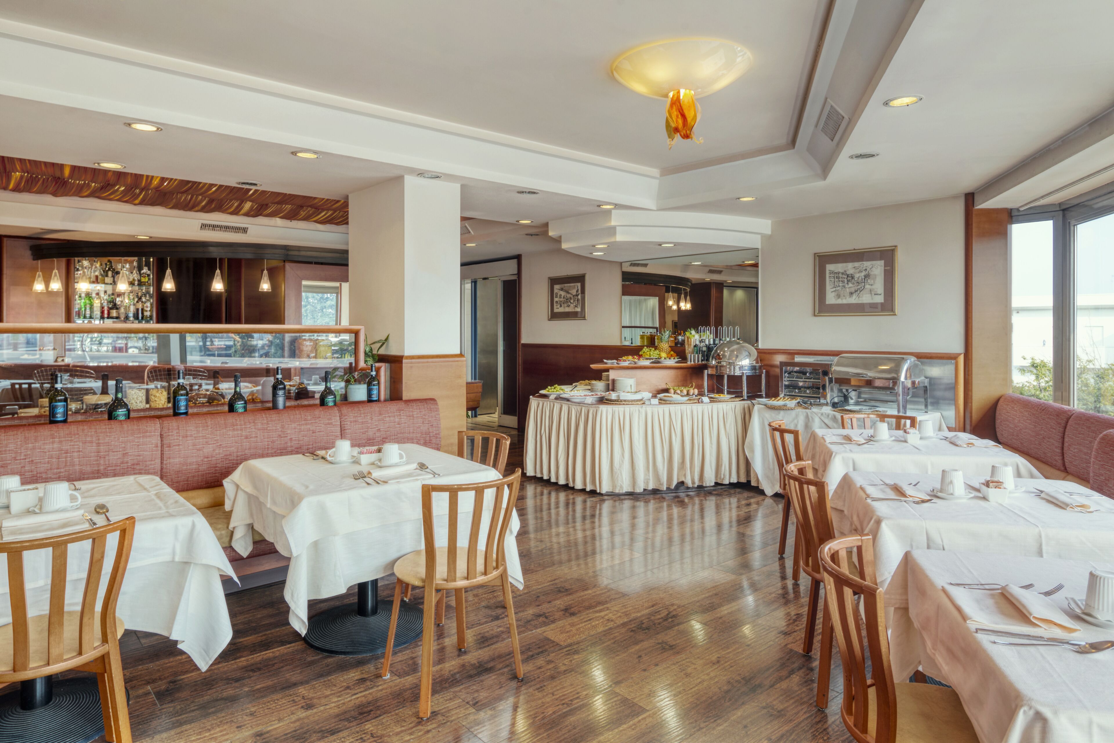 Ein Restaurant mit mehreren Tischen, Sitzecken und einer Theke mit Flaschen sowie einemBuffet.
