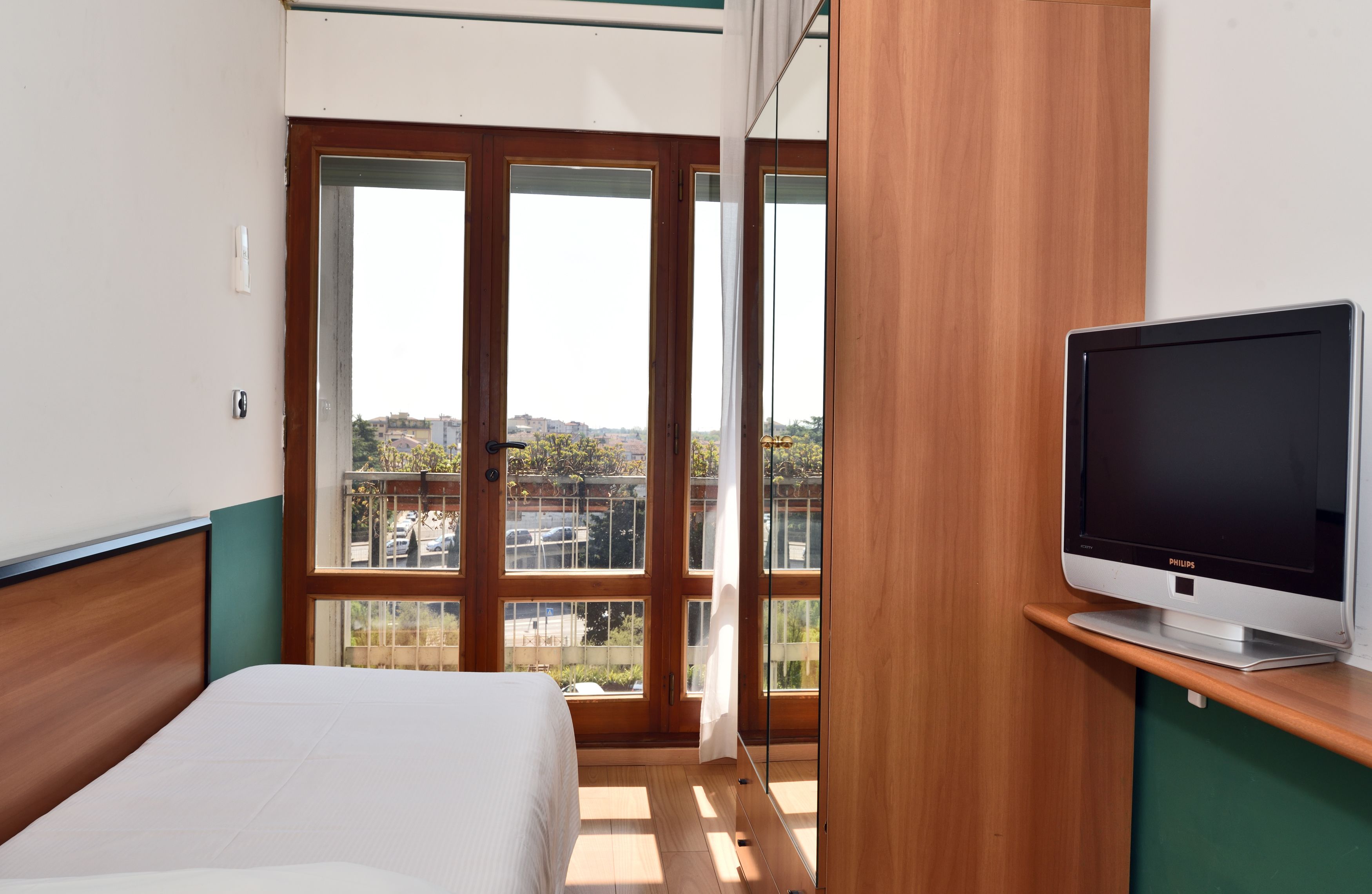 A hotel room with a bed, a television on a stand, and large windows offering a view of the city.