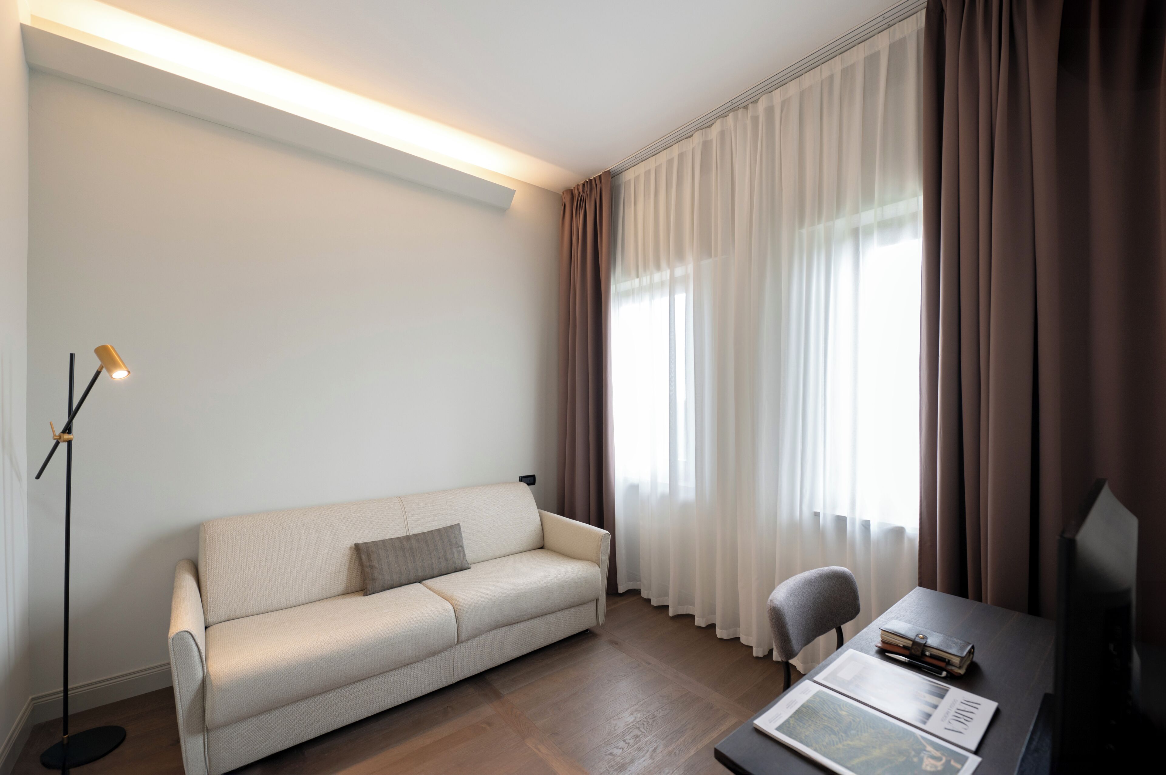 A modern living room with a sofa, a chair, a table with books, and a floor lamp.