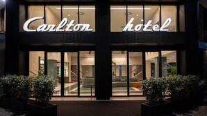 Exterior do Hotel Carlton com fachada moderna, grandes janelas de vidro e uma entrada convidativa.