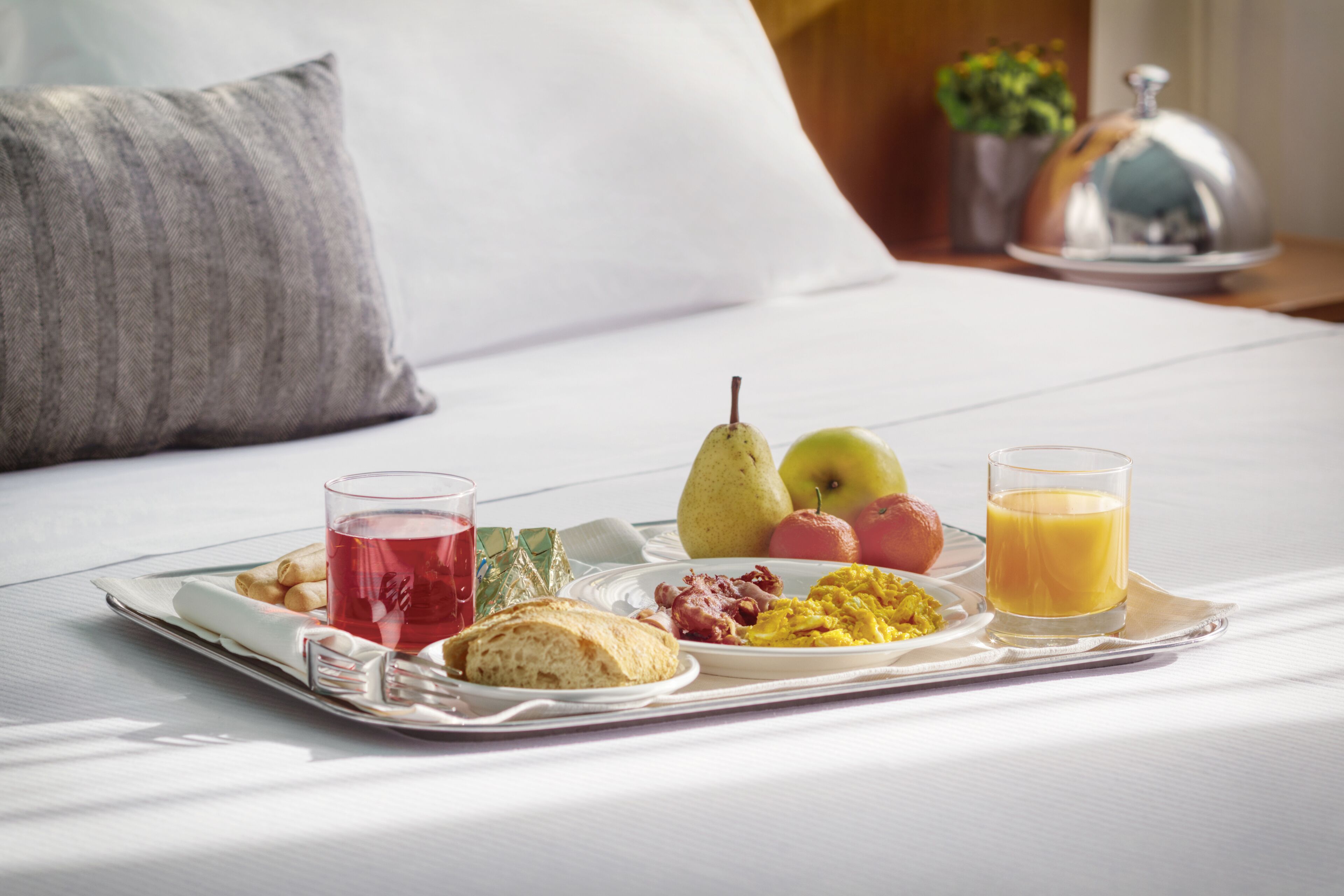 Un plateau de petit-déjeuner sur un lit, avec des œufs, des toasts, des fruits et du jus.