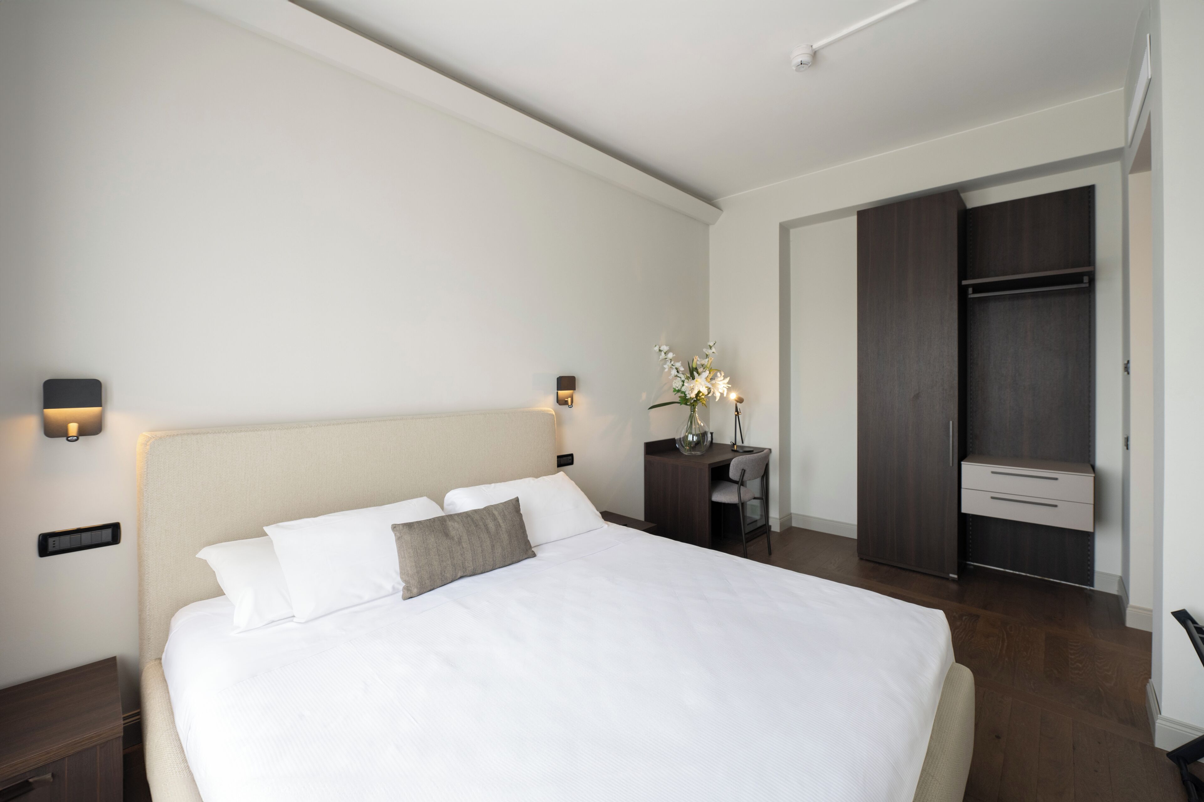 Een moderne slaapkamer met een groot bed, nachtkastjes, een bureau en een kledingkast.