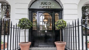A black entrance door with the sign "JUDO HOTEL" above it, flanked by two potted plants.