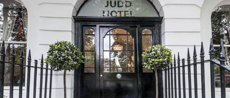 A black entrance door with the sign "JUDO HOTEL" above it, flanked by two potted plants.