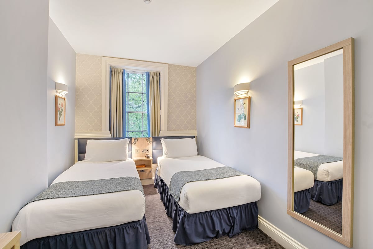 A hotel room with two beds, a large mirror, and a window with curtains.