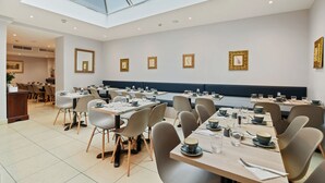 A modern dining area with multiple tables and chairs, a skylight, and framed artwork on the walls.