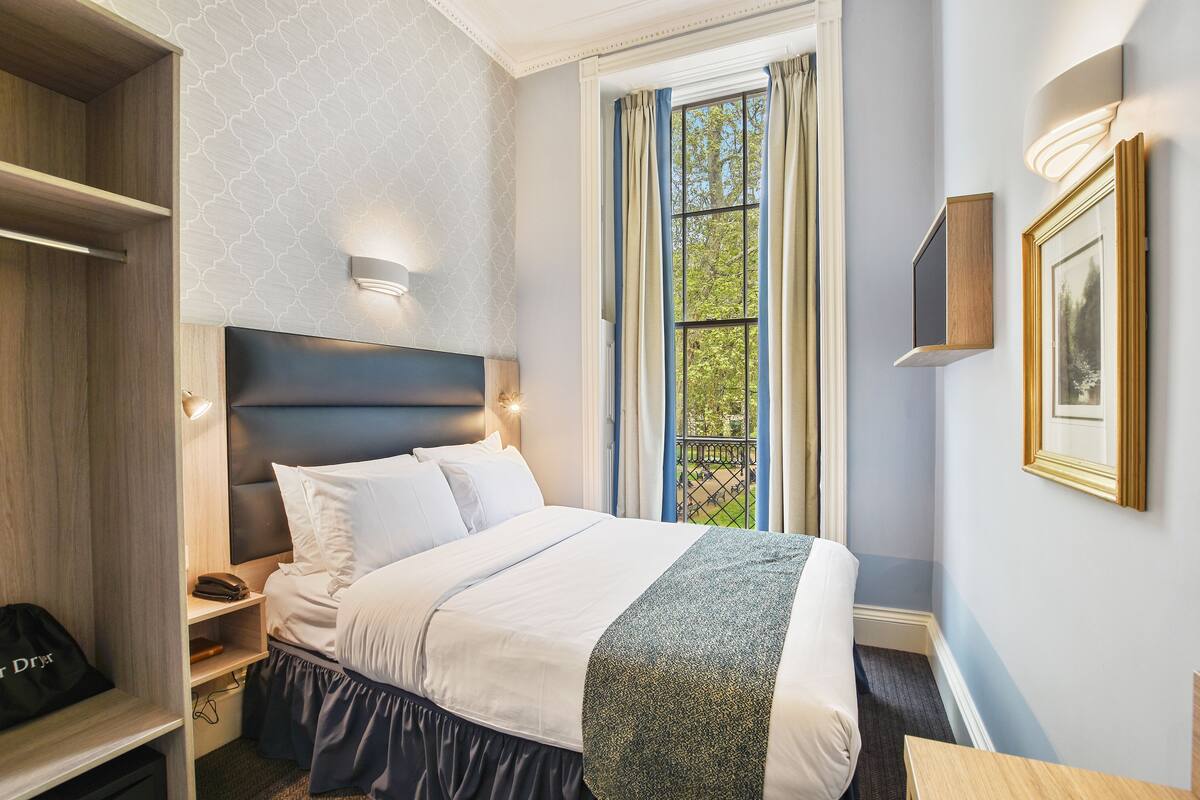 A hotel room with a bed, bedside table, and a window with curtains.