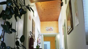 A corridor with a wooden ceiling, tiled floor, and potted plants on the left. - Hotel Ferretti (Florence)
