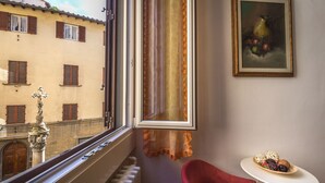 A room with a view of a building, a radiator, a red chair, and a table with decorative items. - Hotel Ferretti (Florence)