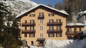 Un hôtel à plusieurs étages doté de balcons, une entrée enneigée et un paysage montagneux en toile de fond.