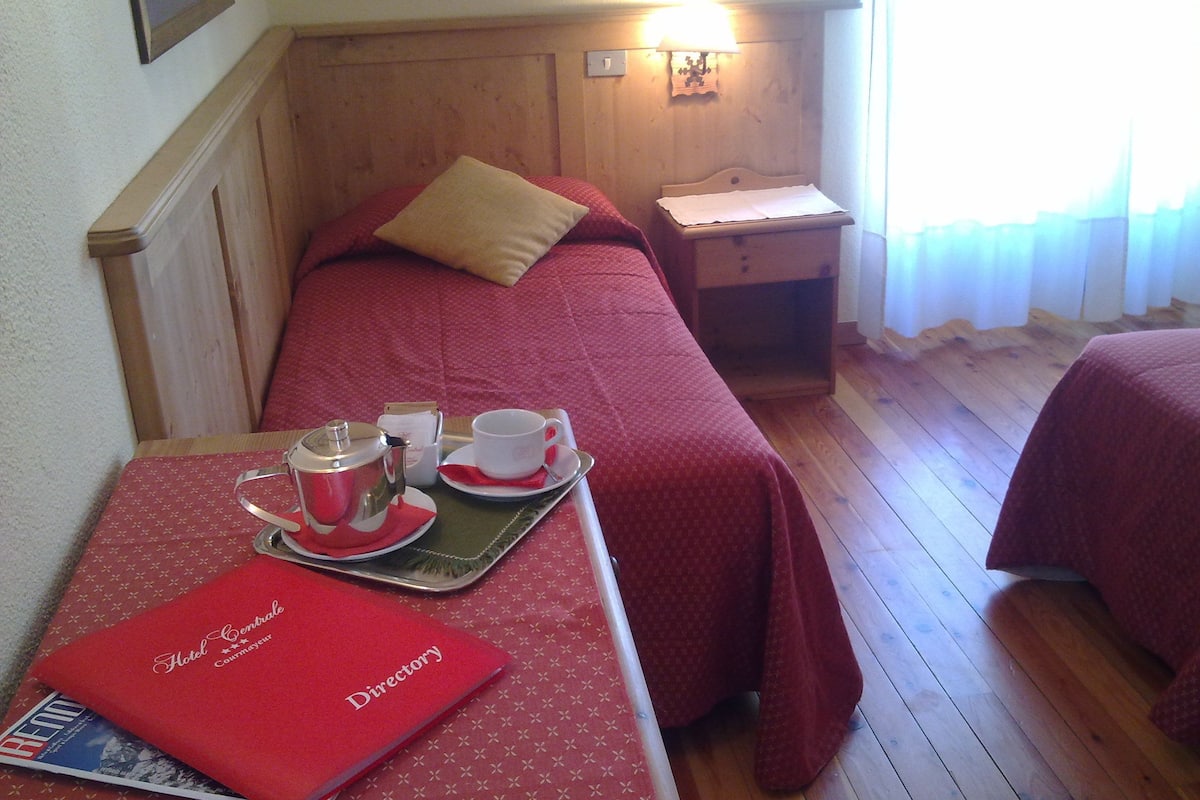 Habitación de hotel con dos camas, una mesita de noche con lámpara, un atril y una bandeja de desayuno con una carpeta roja.