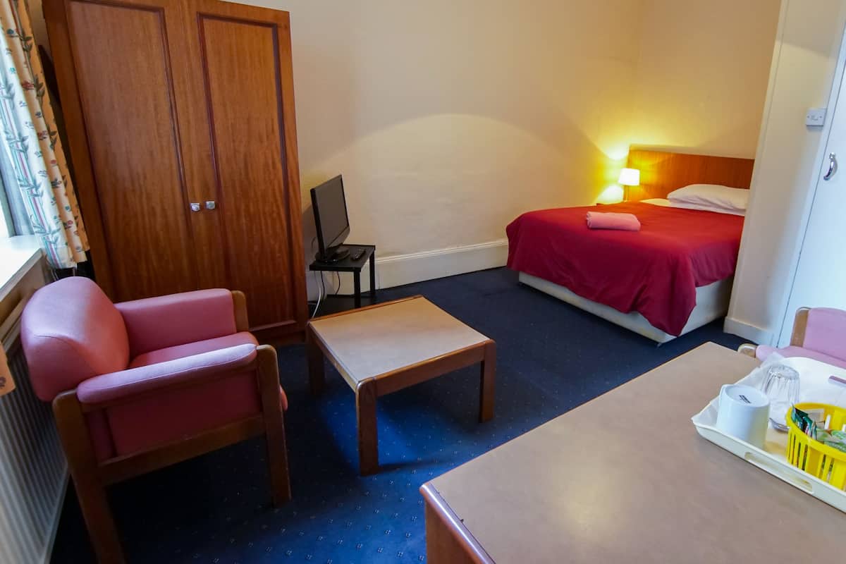 A hotel room with a bed, a desk, a chair, a TV, and a wardrobe.