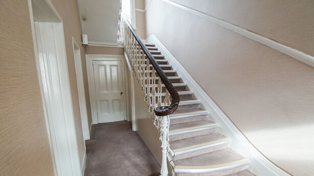 A carpeted staircase with white walls and a white door at the top.