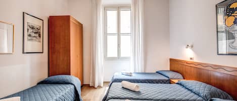Habitación de hotel con dos camas, un armario, una ventana con cortinas e imágenes enmarcadas en las paredes.