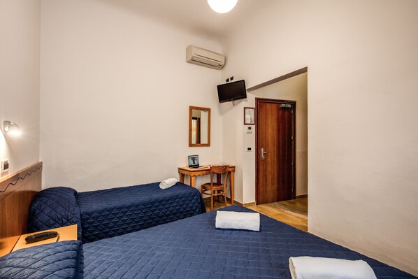 Una habitación con dos camas, un escritorio con computadora, un televisor y una puerta.
