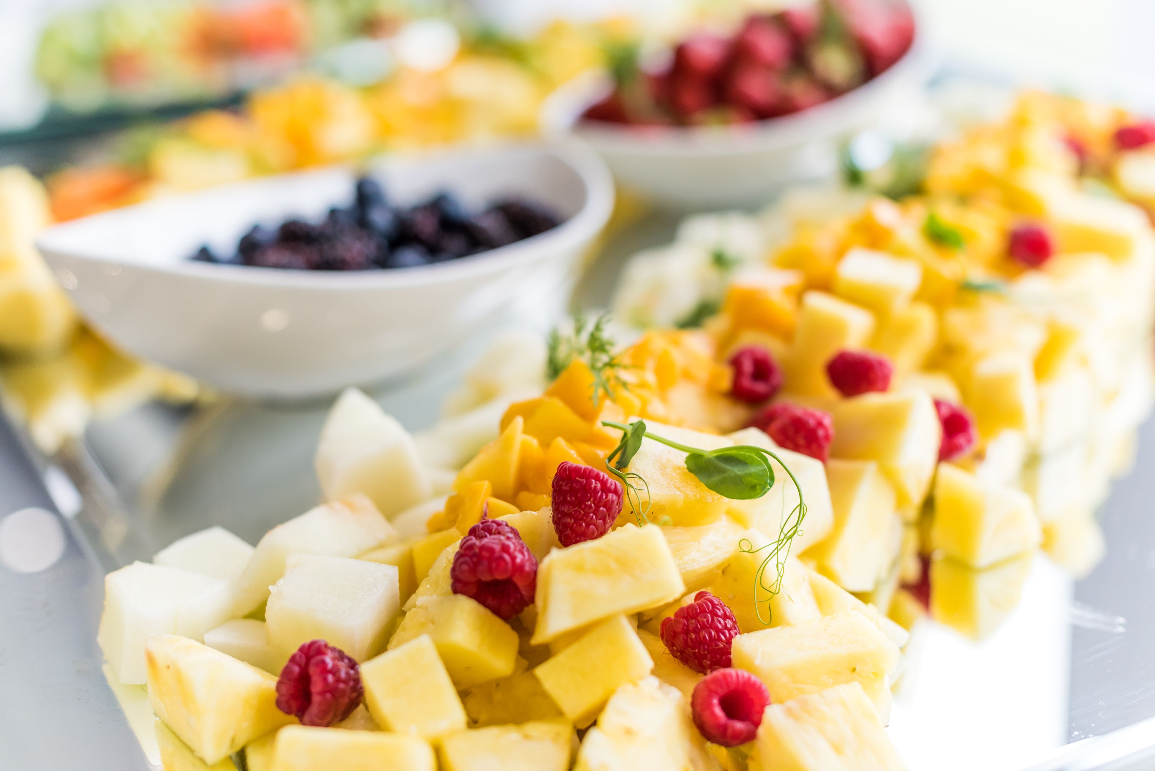 Ensalada de frutas con mango en cubos, frambuesas y una ramita de menta.