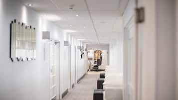 A modern hotel corridor with white walls, a carpeted floor, and a seating area at the end.
