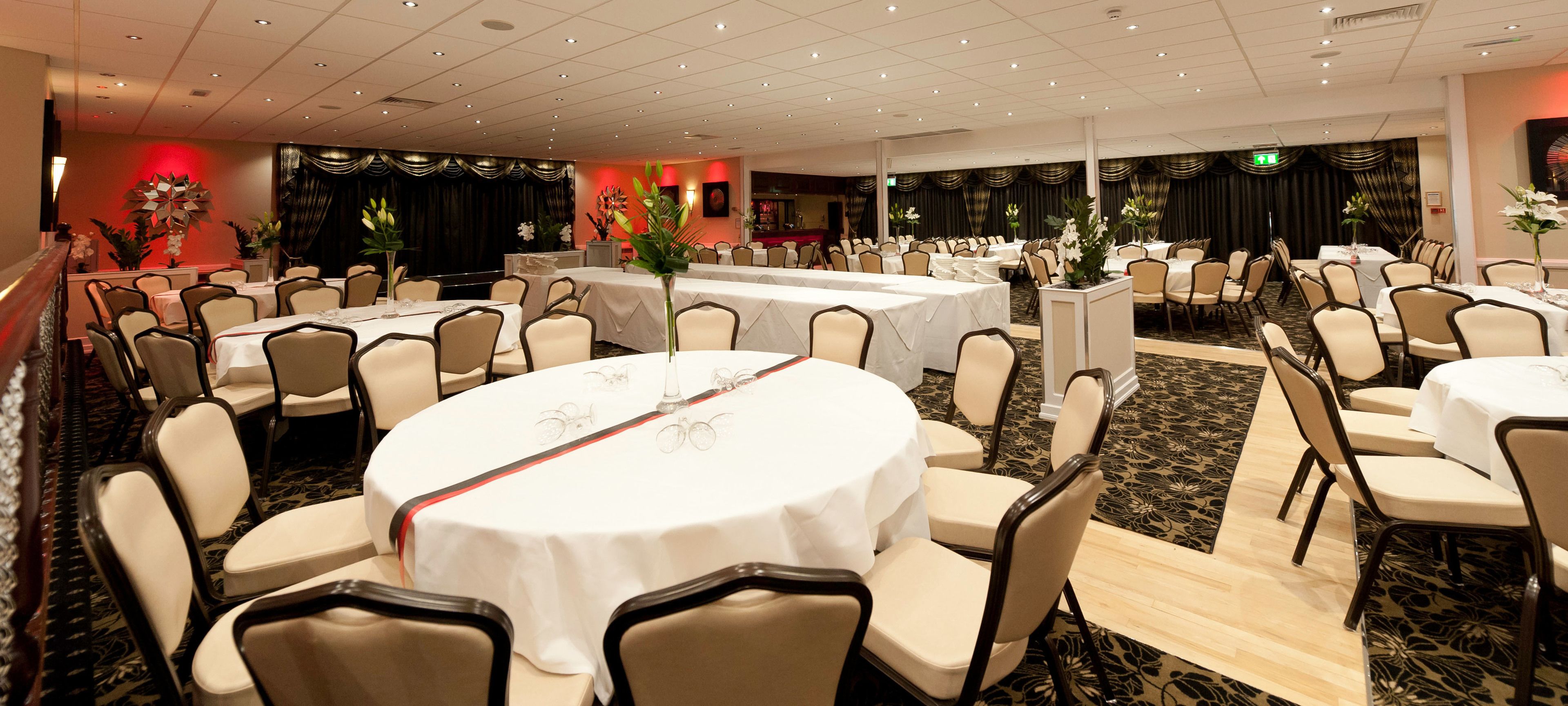 A banquet hall with round tables, chairs, and a stage area.