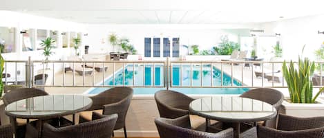 A pool area with wicker chairs and tables, surrounded by potted plants and a glass railing.