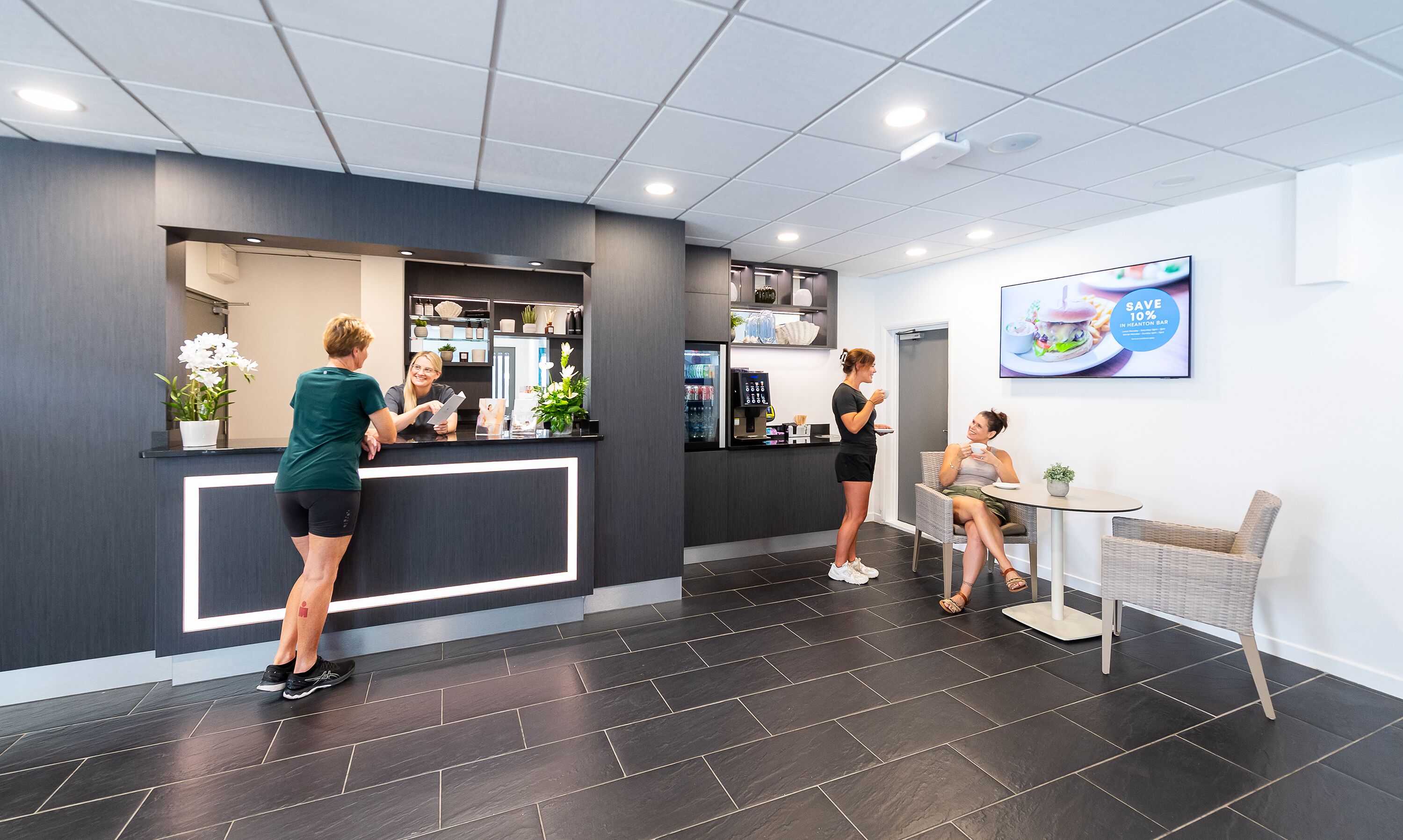 A reception area with a counter, a seating area, and a television screen displaying a promotional image.