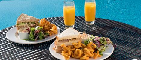 A dining table with plates of food, including sandwiches and salad, and two glasses of orange juice.