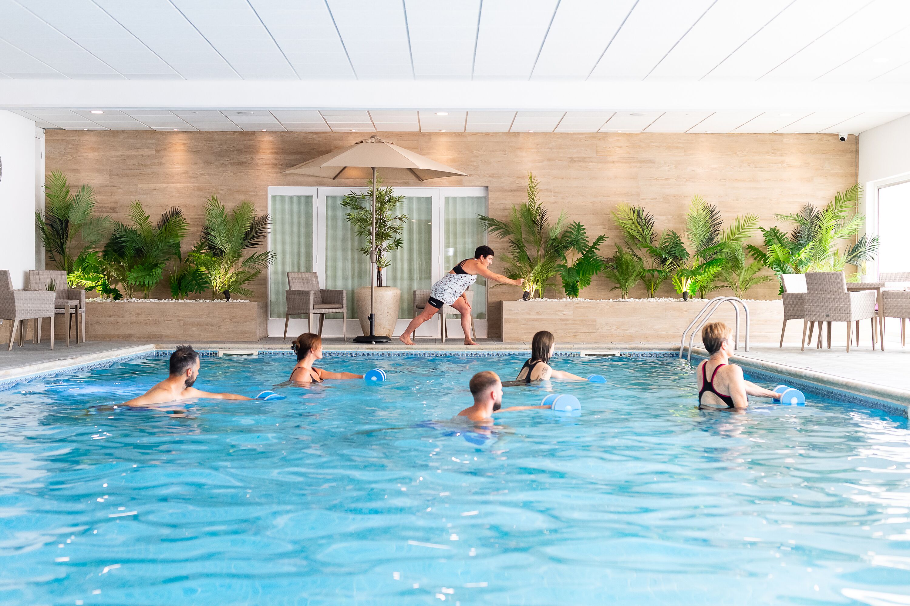 Une piscine intérieure où des personnes nagent, et un sauveteur est présent pour assurer la sécurité.