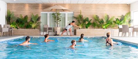 Une piscine intérieure où des personnes nagent, et un sauveteur est présent pour assurer la sécurité.