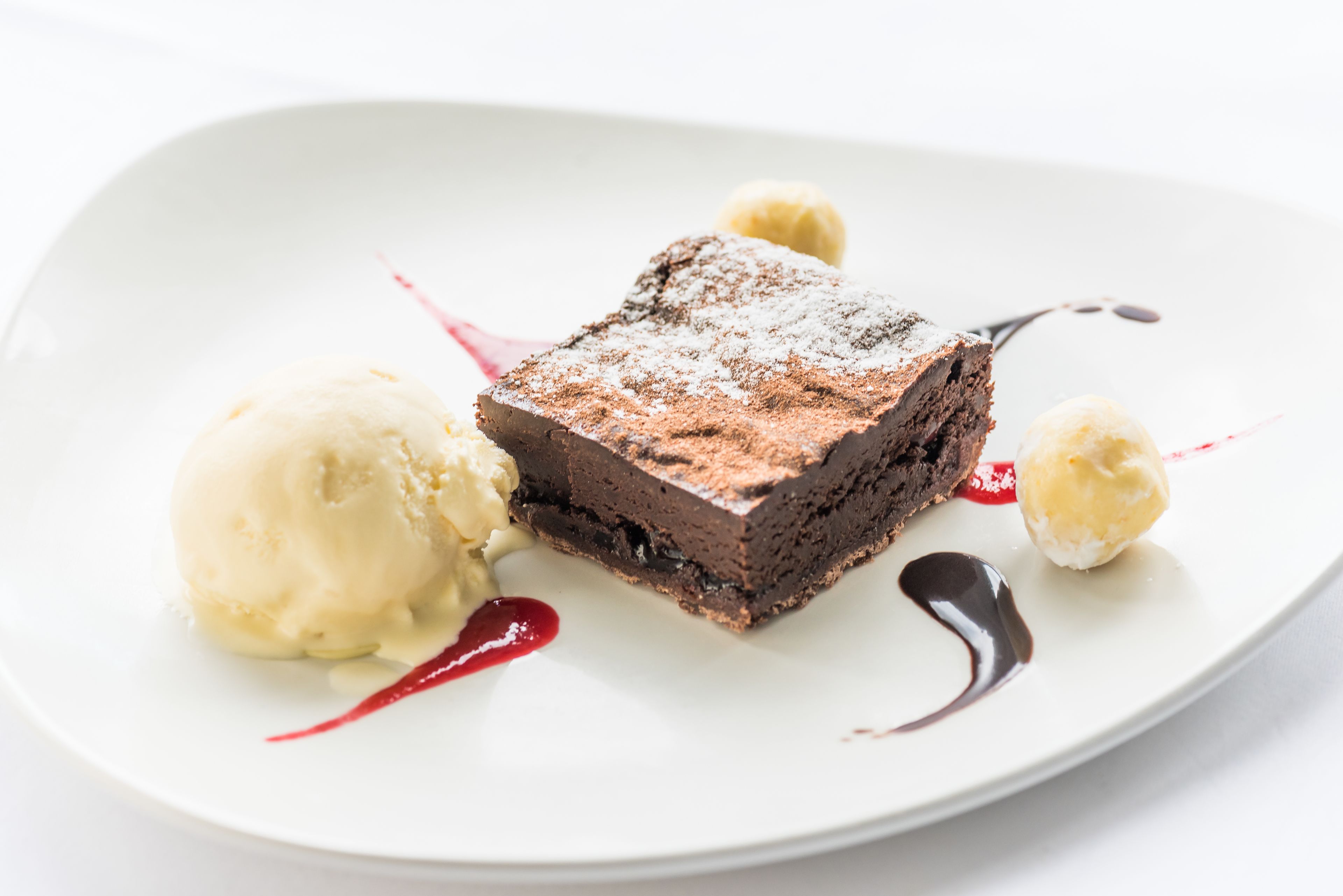 A dessert plate with a slice of chocolate cake, a scoop of vanilla ice cream, and a small dollop of cream.