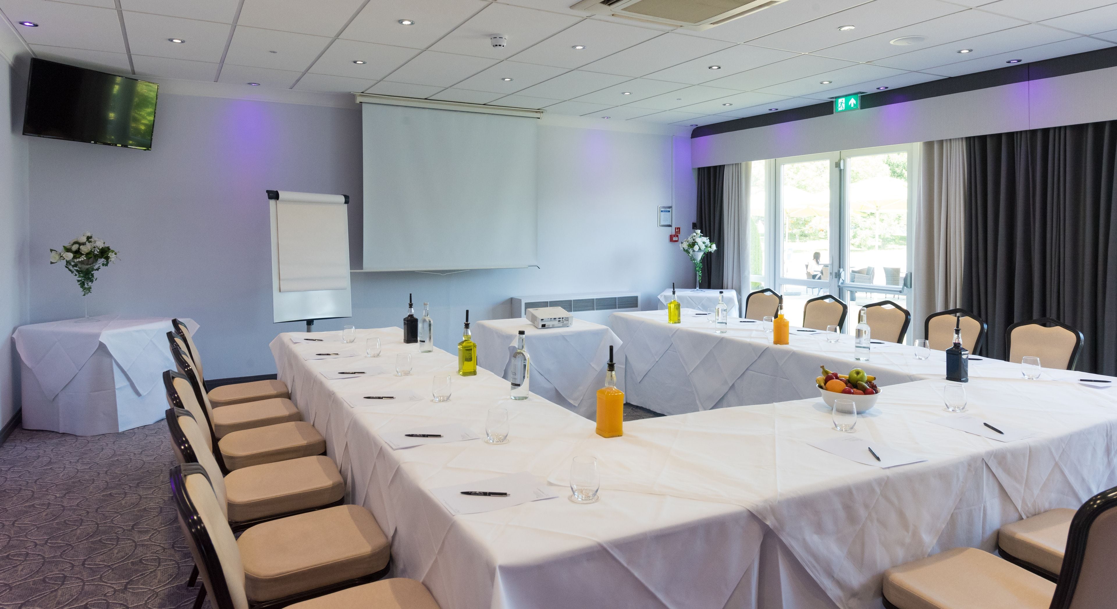 A conference room with a long table, chairs, a projector screen, and a large window.